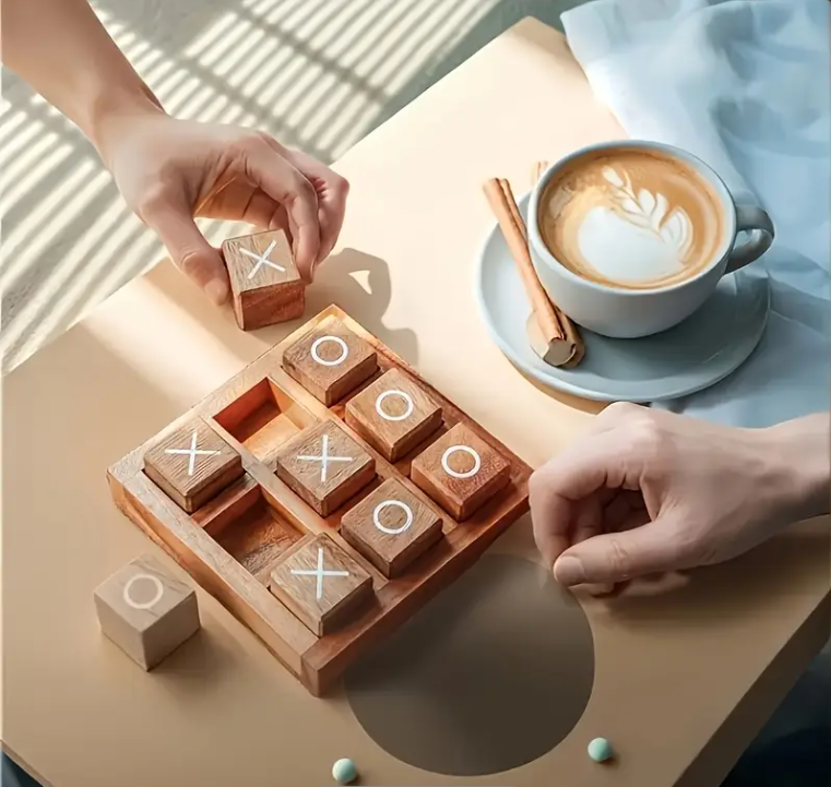 Wooden tic-tac-toe game with hands playing, next to a cup of coffee on a table.